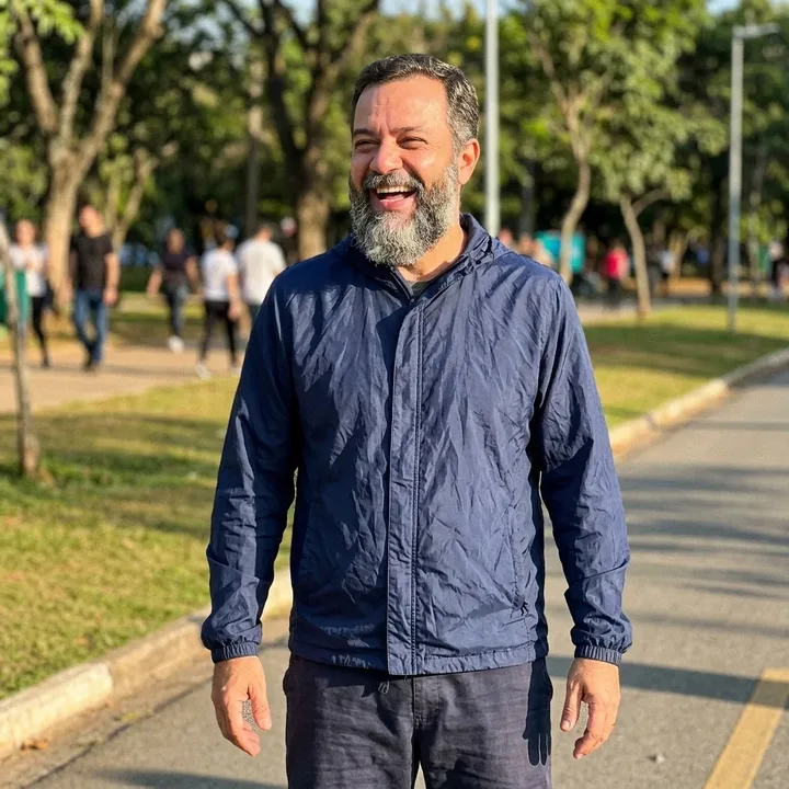 A smiling man in a blue jacket walking outdoors in a park